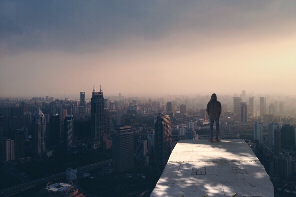 شاب يقف وحيدًا على قمة مبنى وينظر إلى المدينة