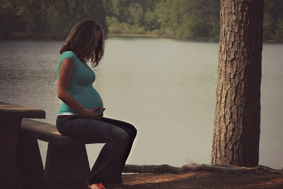 امرأة حامل تجلس بالقرب من النهر وتمسك ببطنها