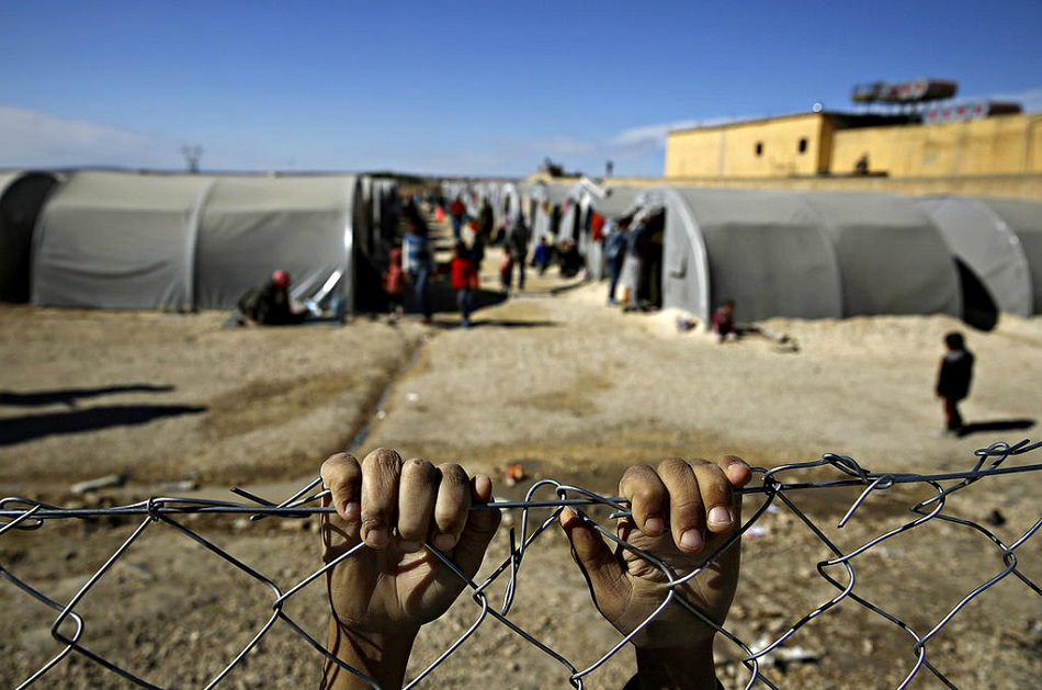 لاجئ يتشبث بسور من السلك يفصل المخيم عمَّا وراءه
